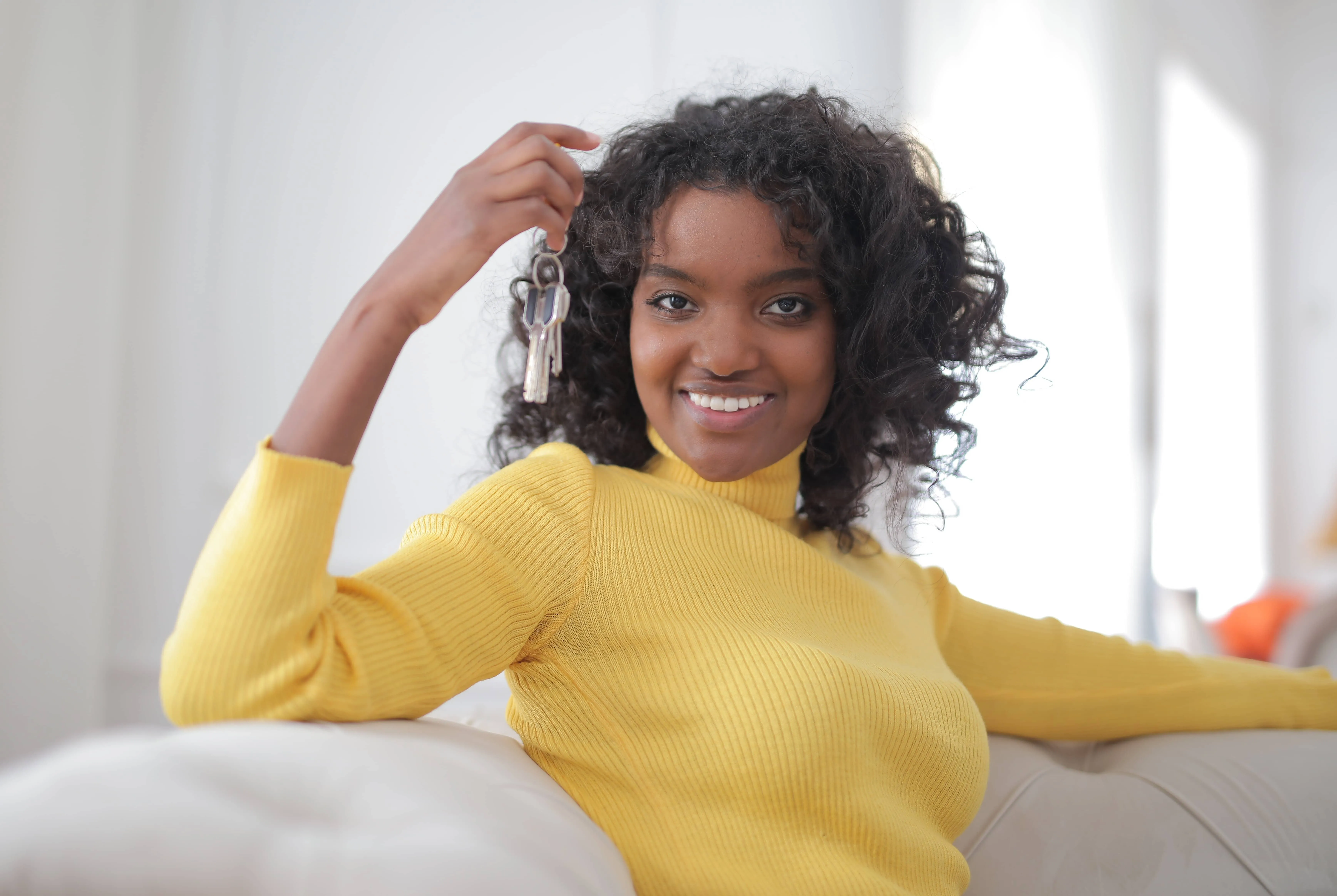 A young woman smiling, holding keys in her hand, symbolizing the joy of moving into a new home.